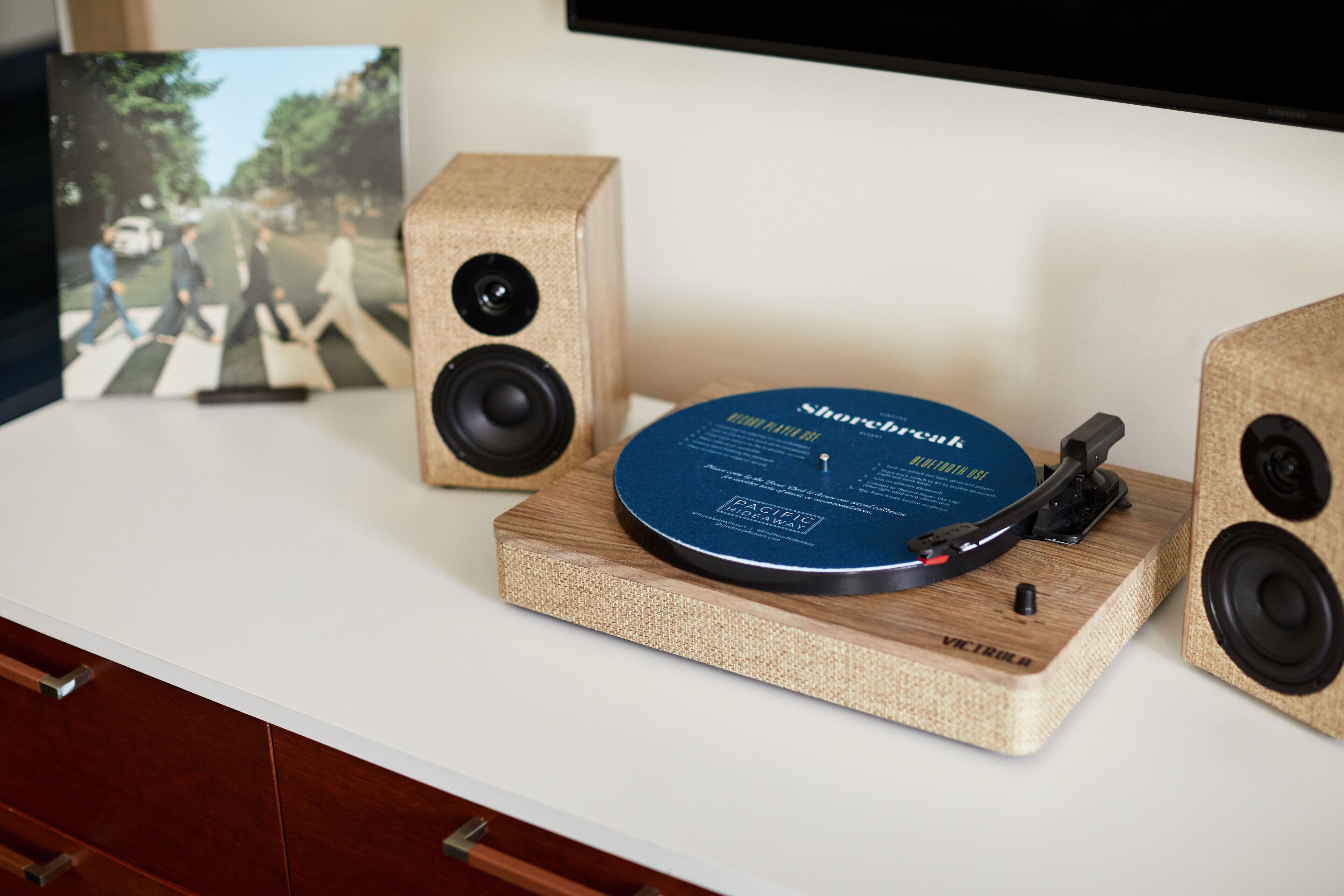 Een draaitafel met een vinylplaat op een houten standaard, samen met twee speakers.