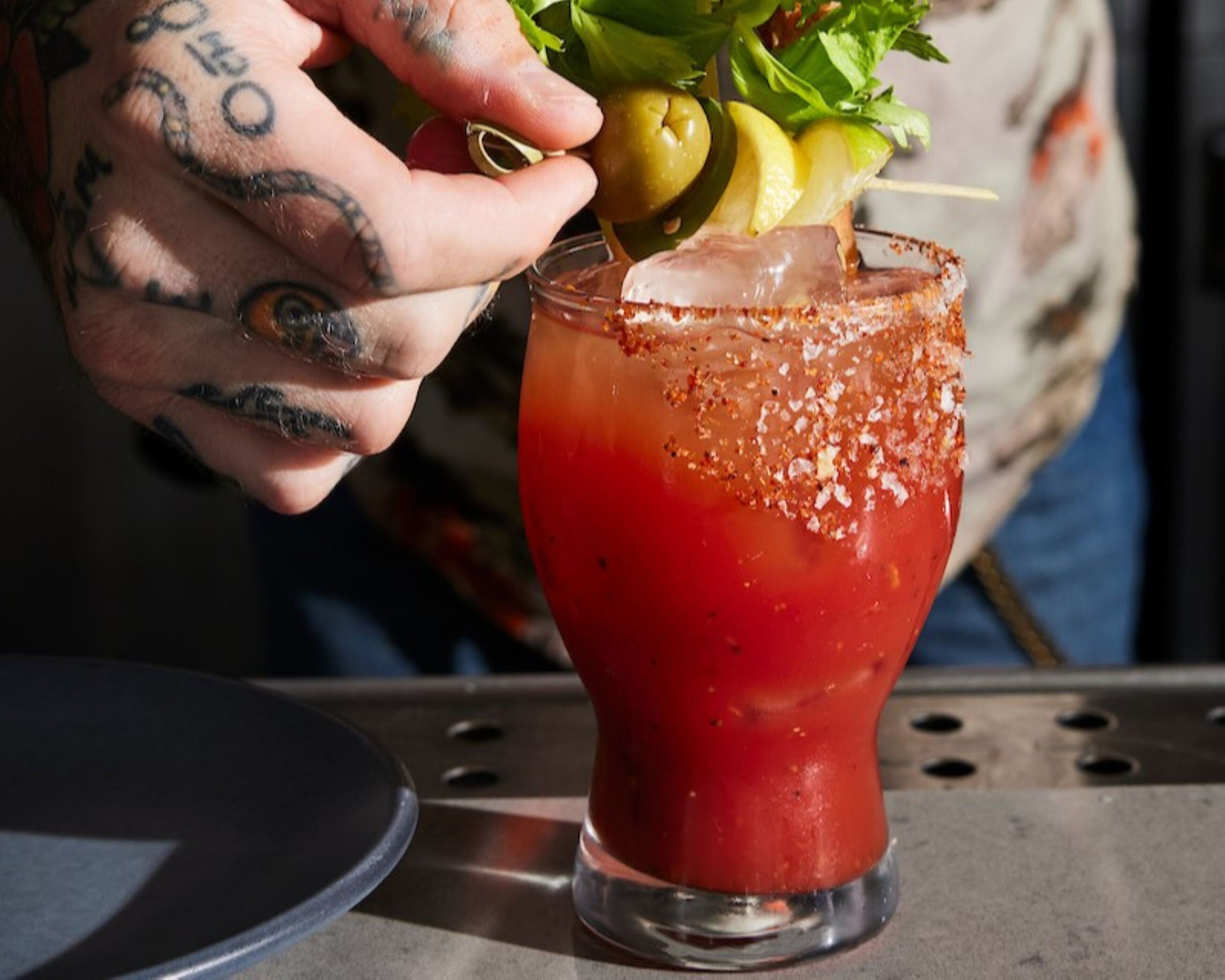 A cocktail with a salted rim, garnished with a lemon and herbs, served in a glass.