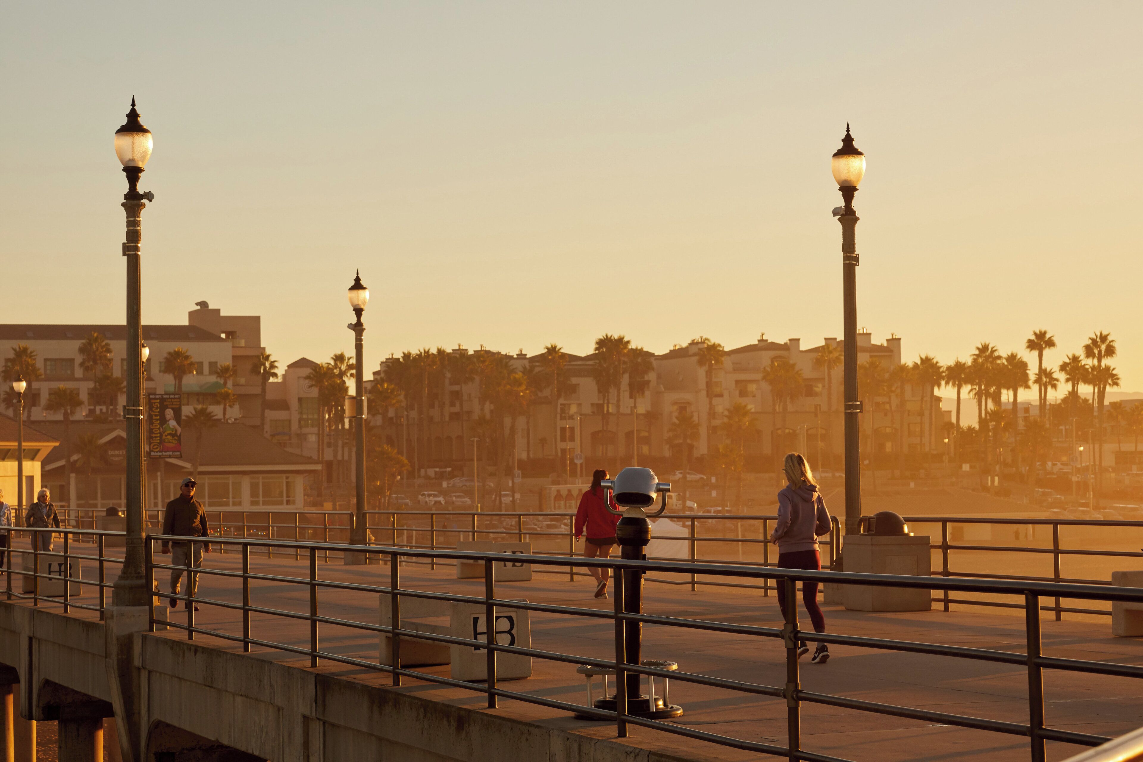 A pedestrian bridge with street lamps, palm trees, and buildings in the background.