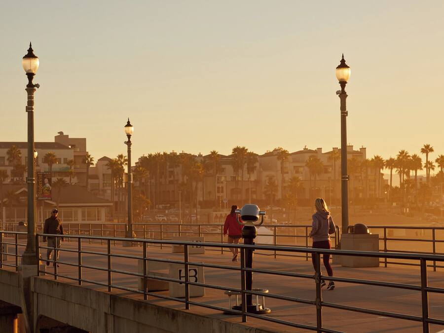 A pedestrian bridge with street lamps, palm trees, and buildings in the background.