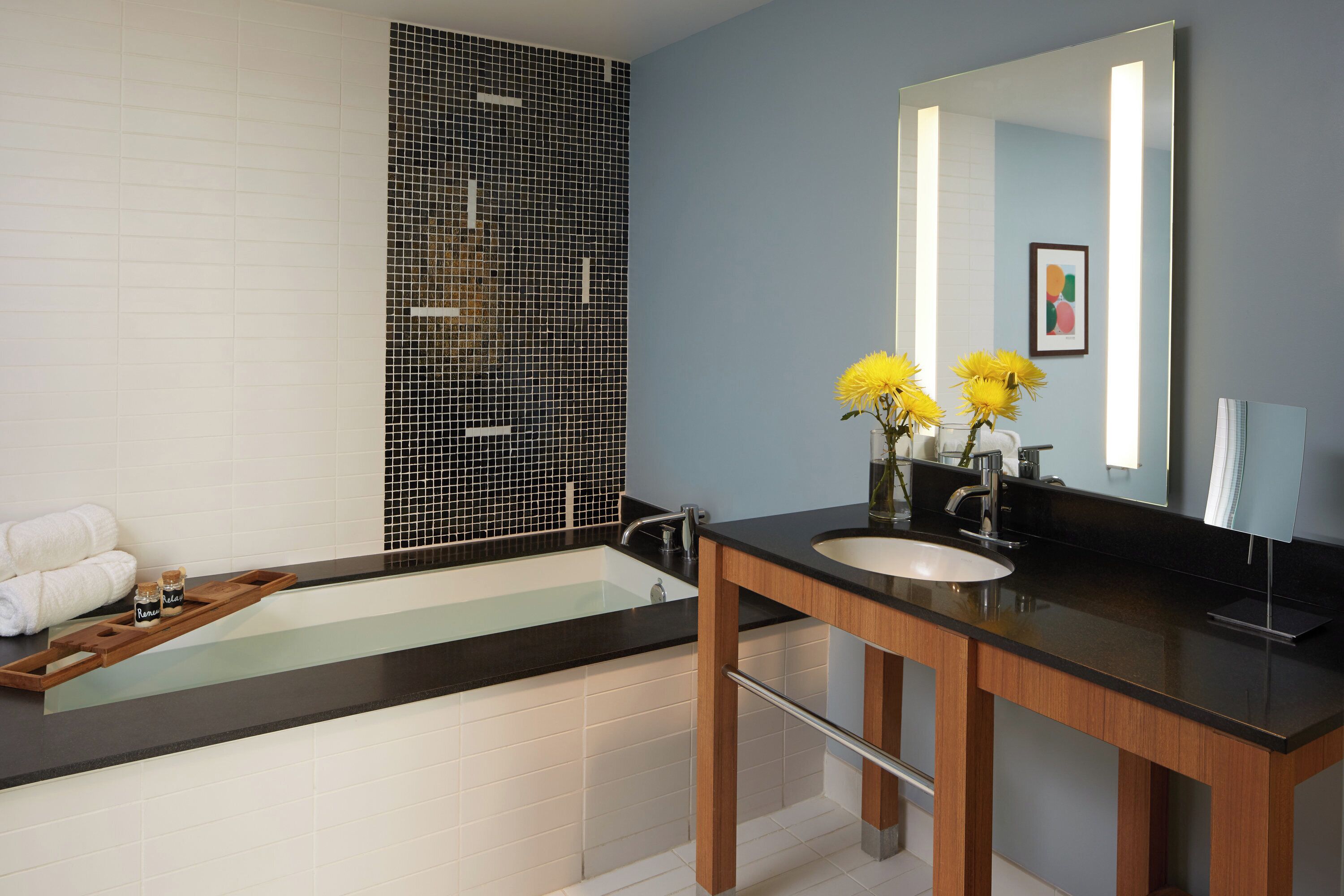 A modern bathroom with a bathtub, a vanity with a mirror, and a tray with toiletries.
