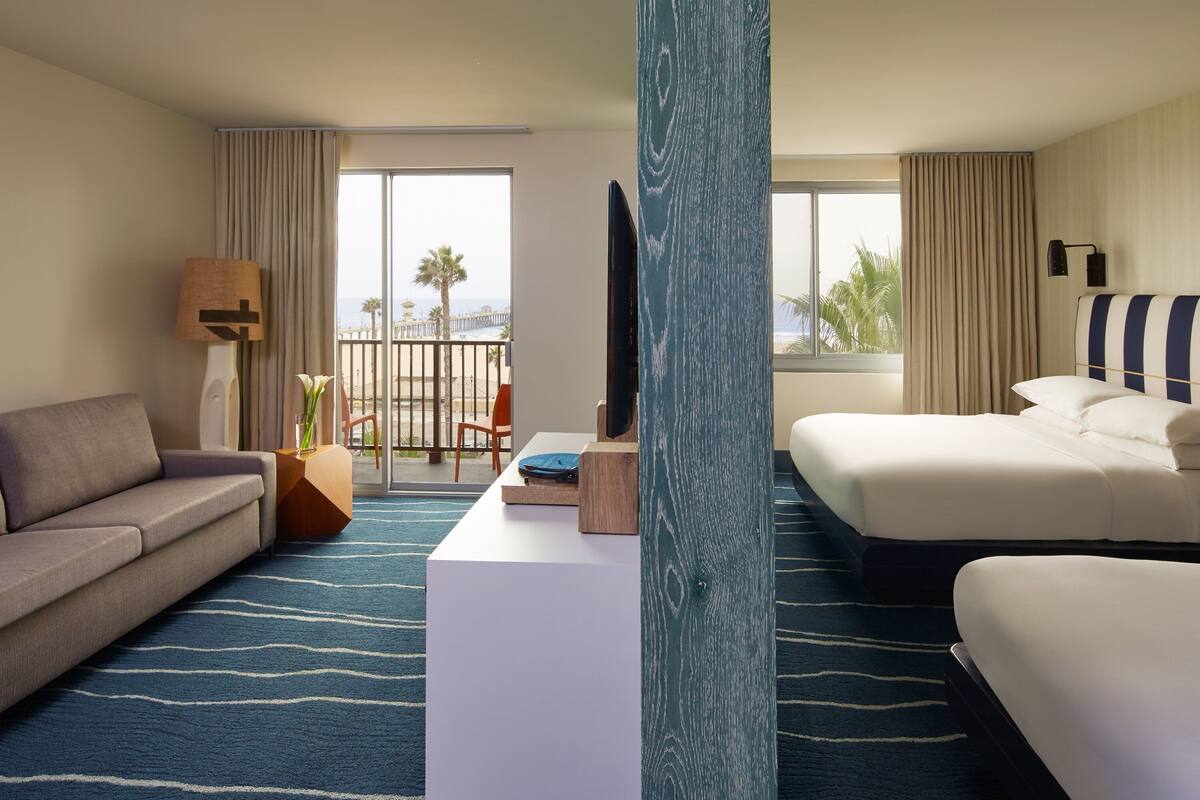 A hotel room with a sofa, a bed, a desk, and a view of the balcony.
