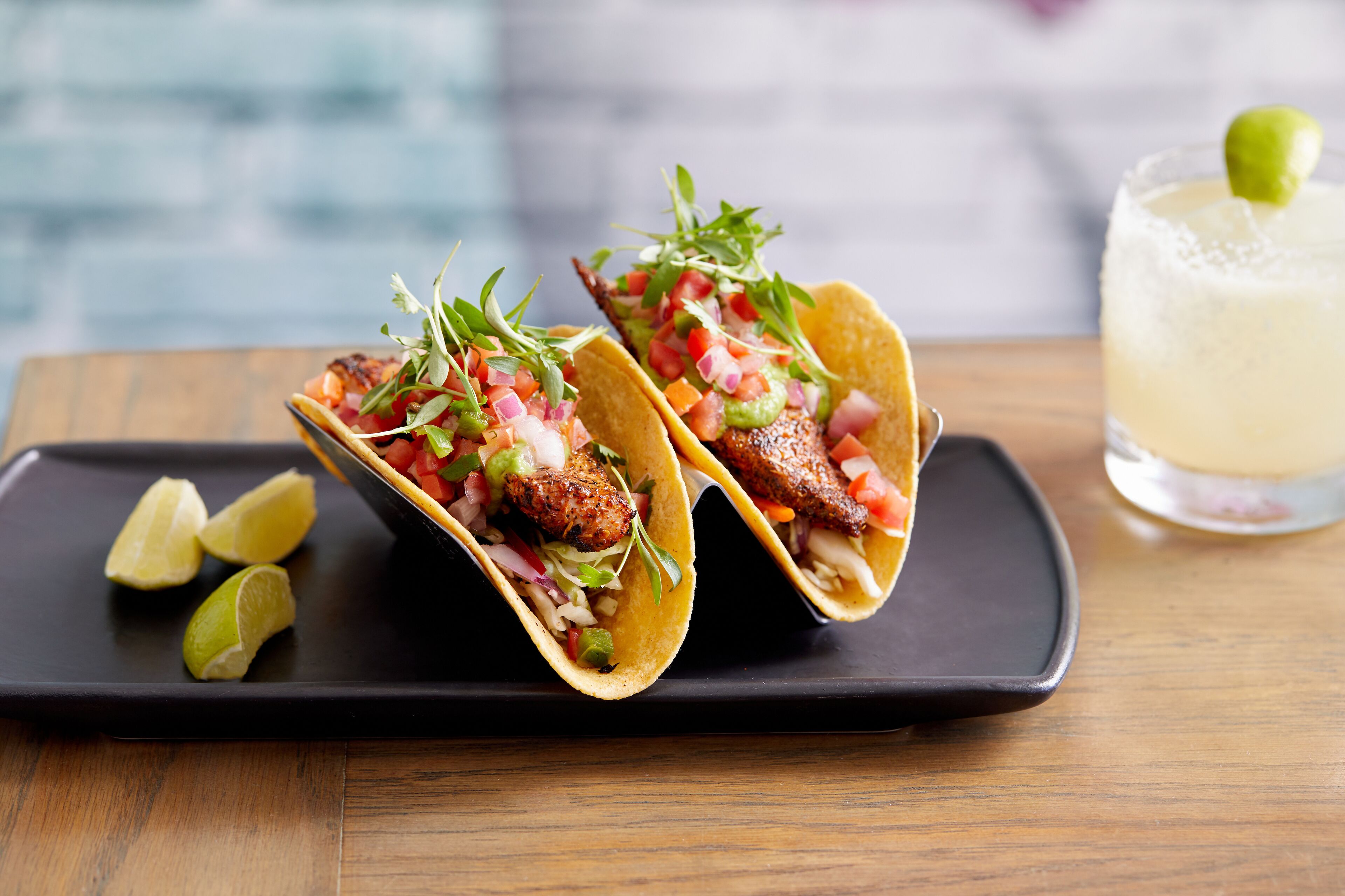Dos tacos con ingredientes y una bebida sobre un plato negro.