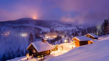 A snow-covered mountain village at night with wooden cabins and a warm glow from the windows.
