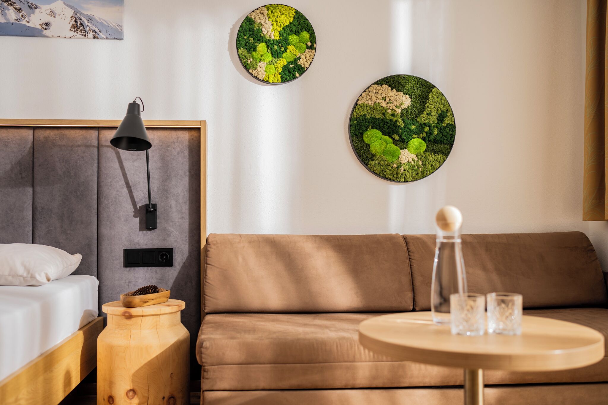 Una habitación de hotel moderna con una cama, una mesita de noche de madera, una mesa redonda con vasos y dos obras de arte circulares en la pared.