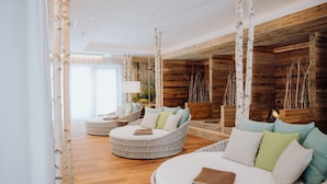 Un moderno spa con una pared de madera, una cama redonda con almohadones y un abedul blanco en la esquina.