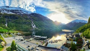 A lakeside village with buildings and boats, surrounded by mountains and greenery. - Havila Hotel Geiranger (Stranda)