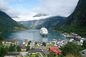 A cruise ship docked at a port with a mountainous backdrop and a small town in the foreground.