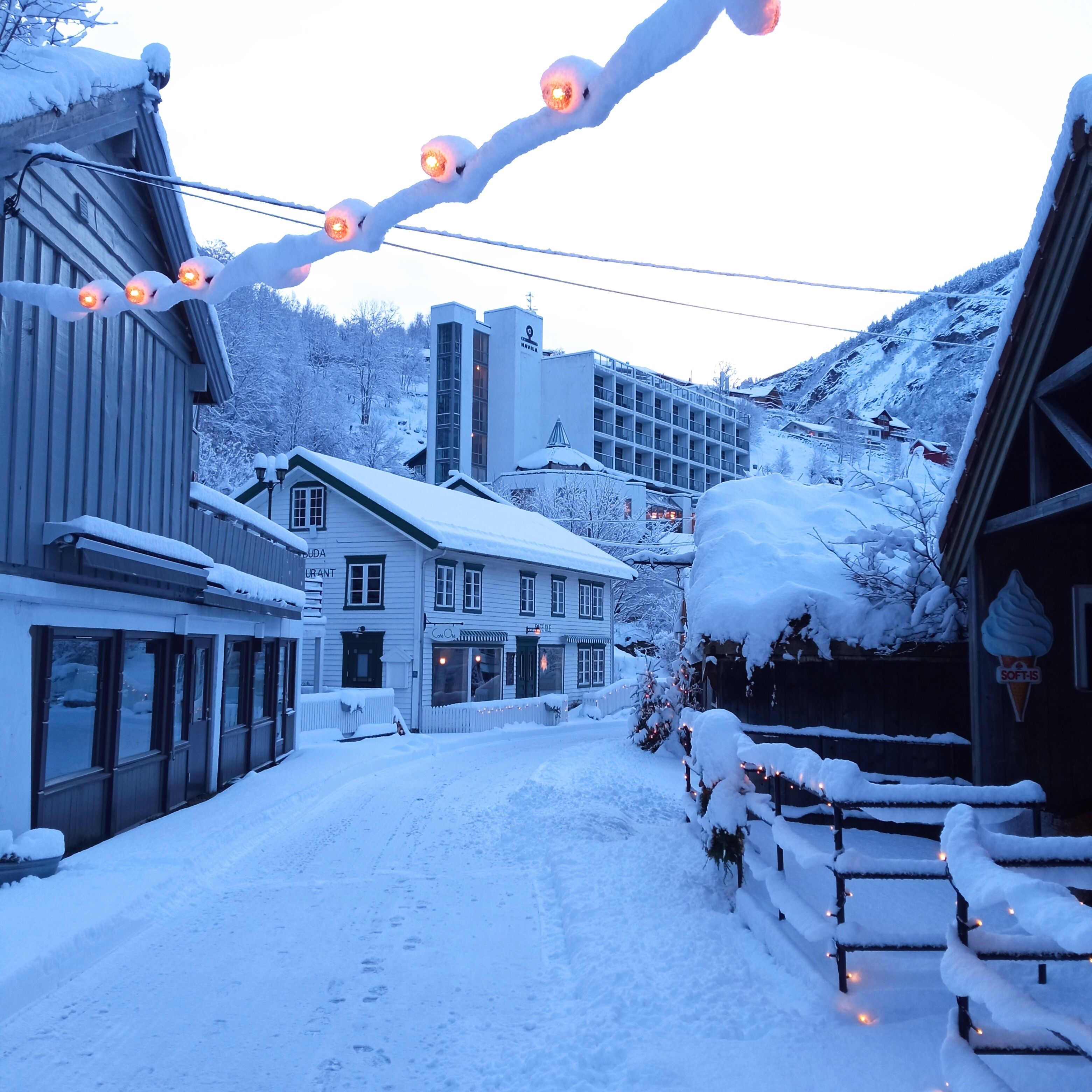 A snow-covered street with buildings, including a hotel and a restaurant.