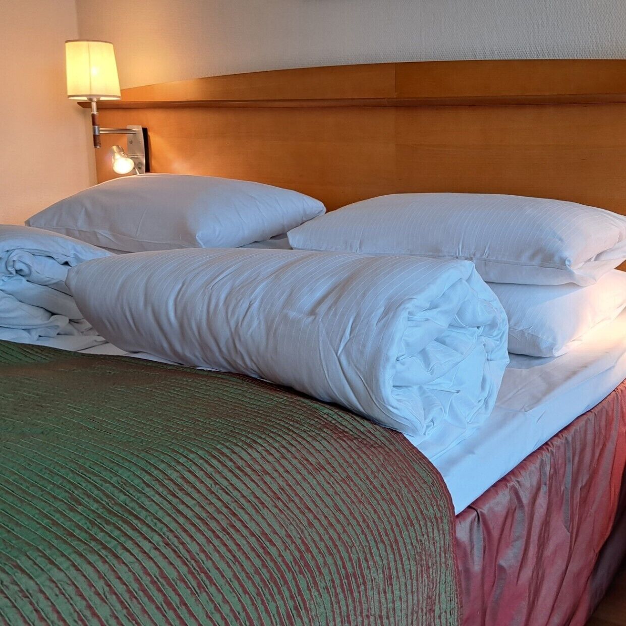 A neatly made bed with white linens and a green striped blanket, a wooden headboard, and a bedside lamp.