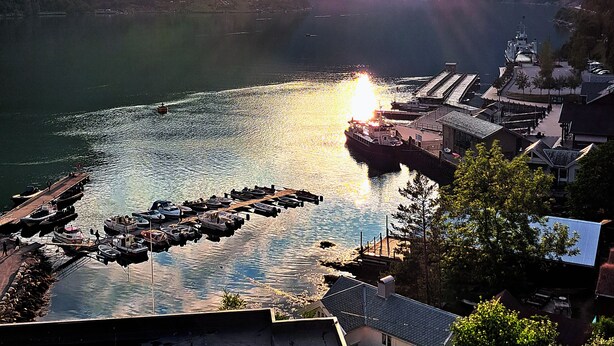 A lakeside view with a dock, boats, and a mountainous backdrop. - Havila Hotel Geiranger (Stranda)