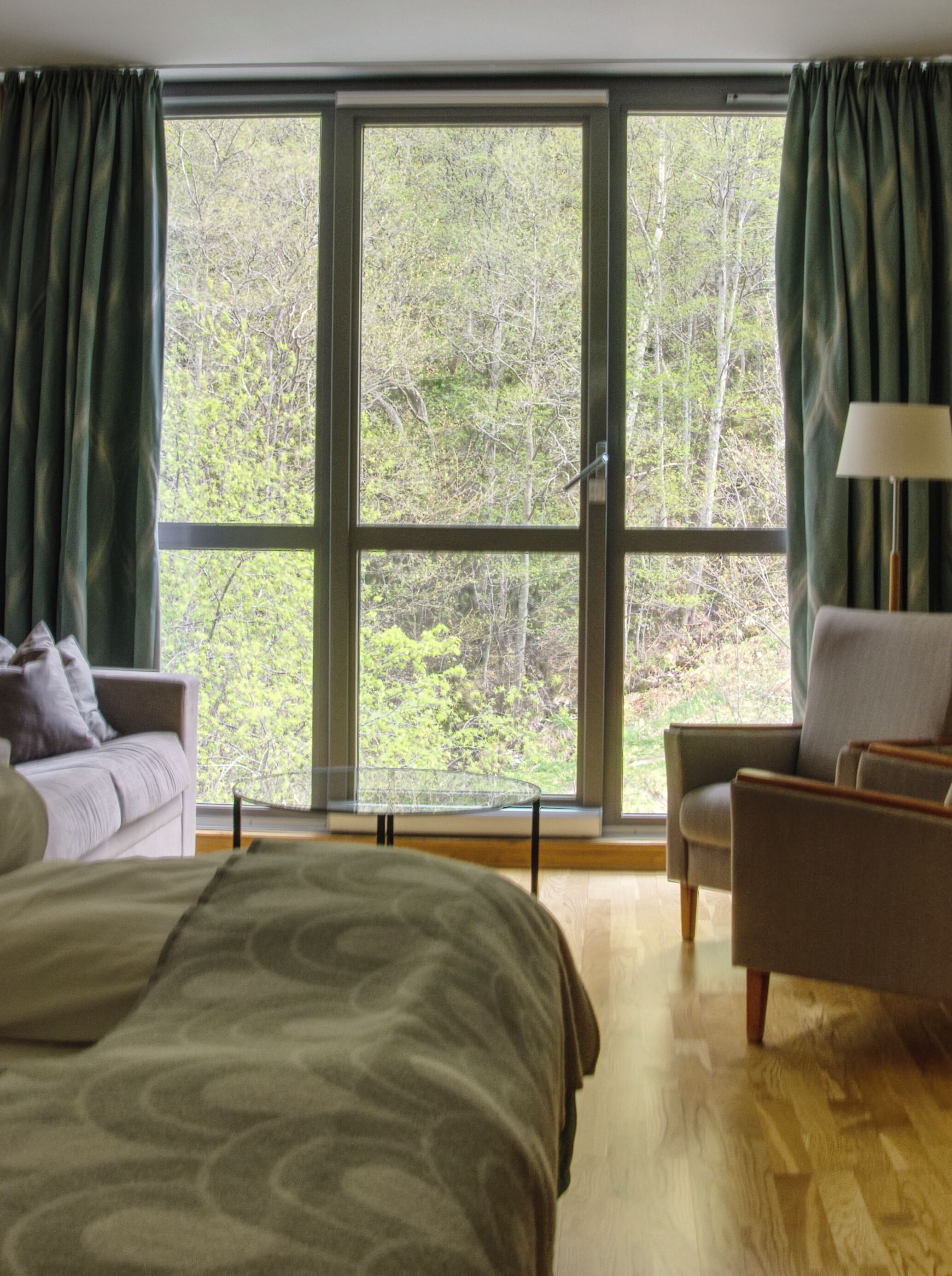A bedroom with a large window, a bed, a chair, and a lamp.