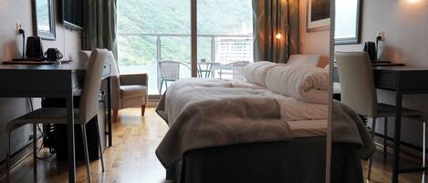 A hotel room with a bed, two chairs, a desk, and a view of a mountainous landscape.