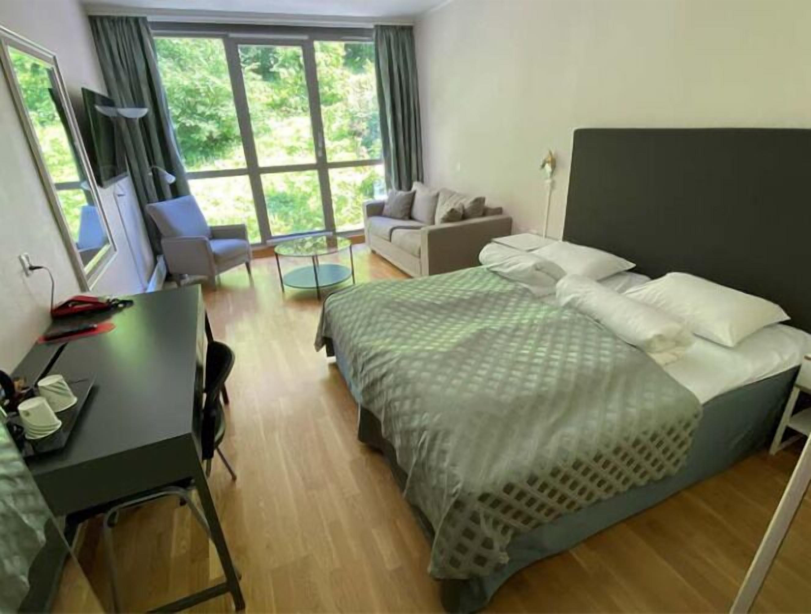 A hotel room with a bed, a desk, a chair, a sofa, and a window with curtains.