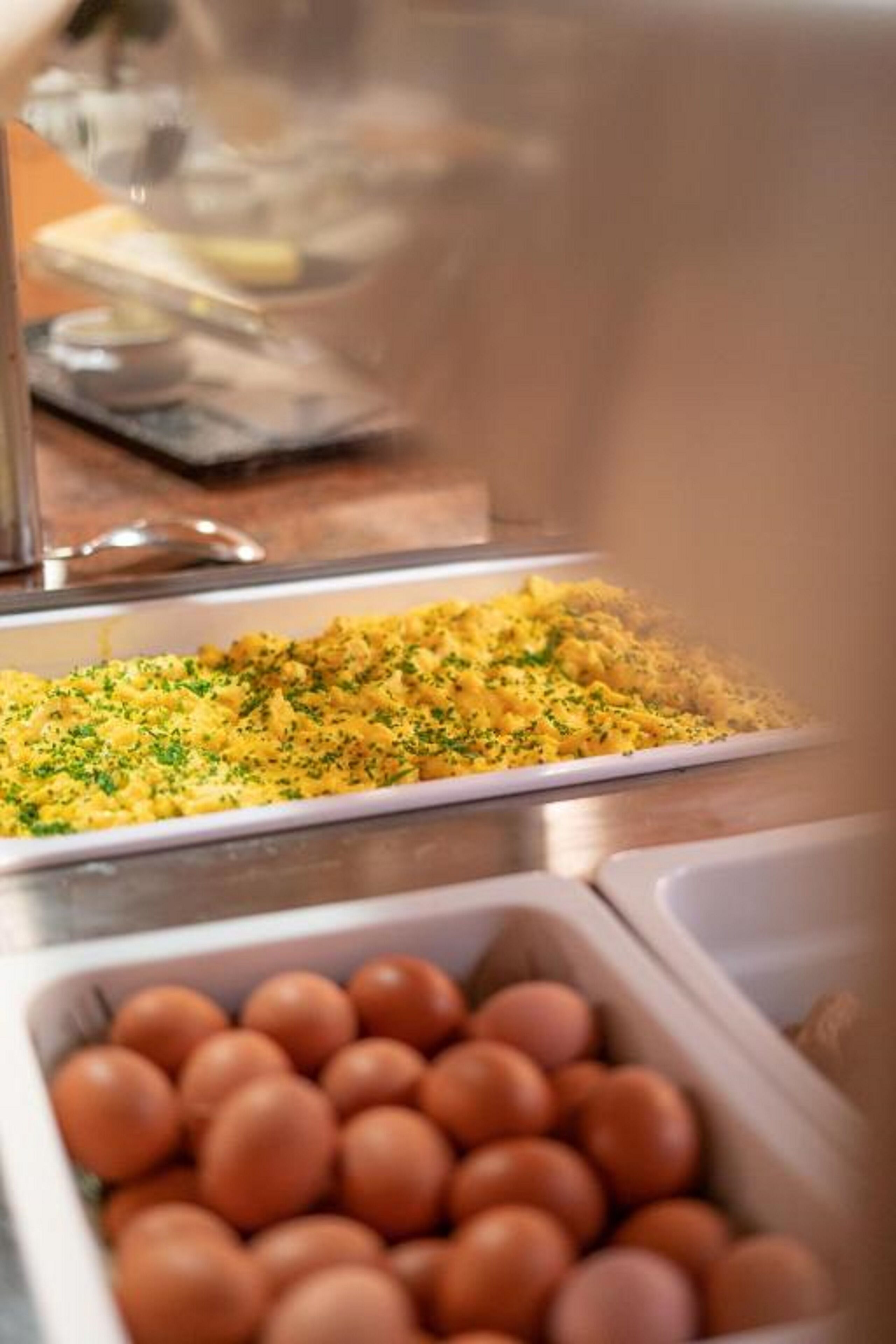 A buffet with scrambled eggs and a container of eggs.
