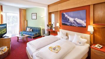 A hotel room with a bed, a sofa, a desk, a television, and a painting on the wall.