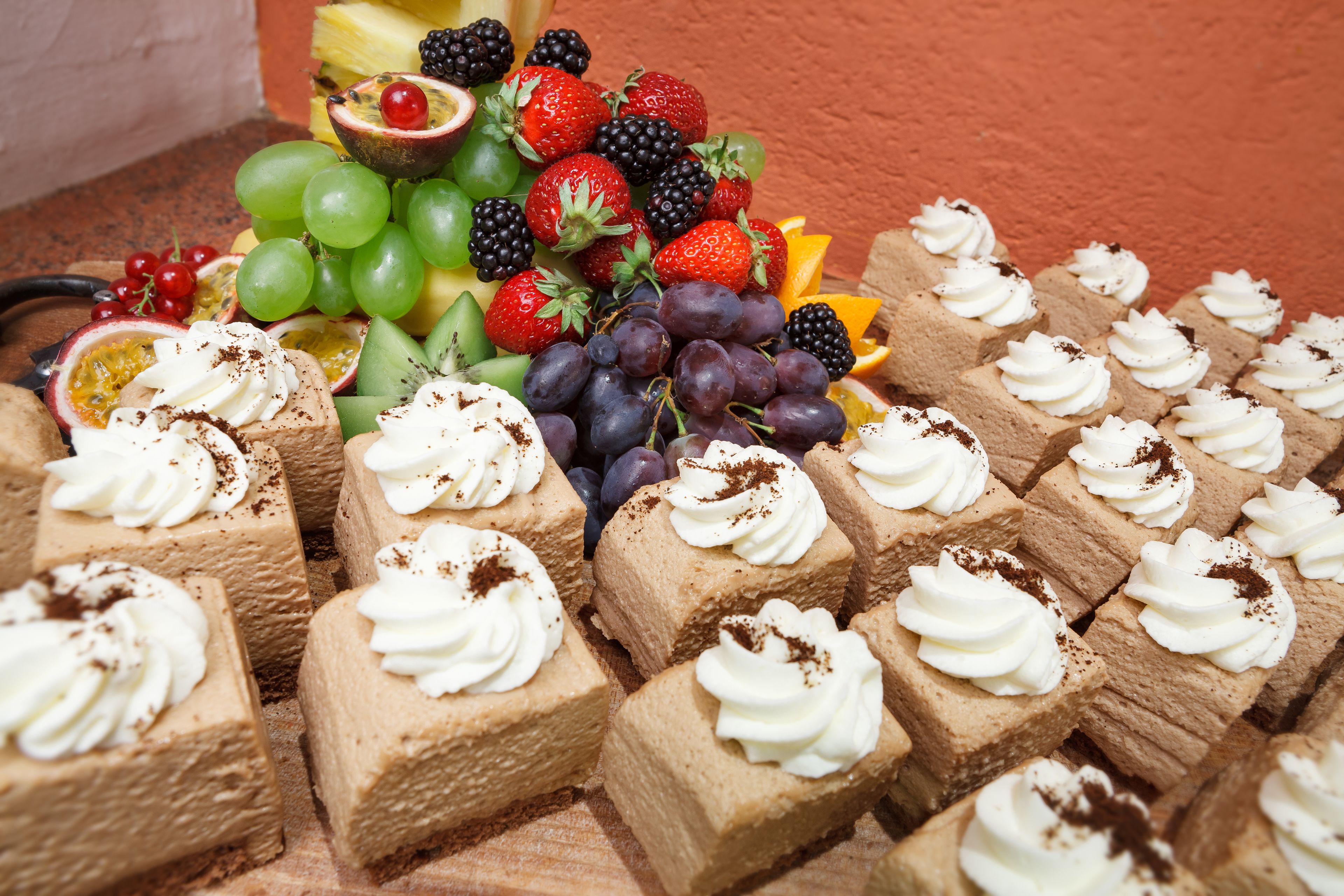 Una variedad de postres y frutas dispuestas sobre una mesa de madera frente a un muro rojo.