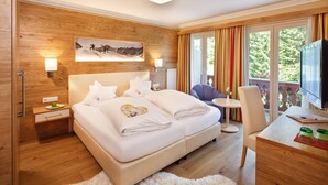 Une chambre d’hôtel moderne avec un mur d’accent en bois, un grand lit avec du linge de lit blanc, un bureau avec une télévision et un balcon avec des rideaux.
