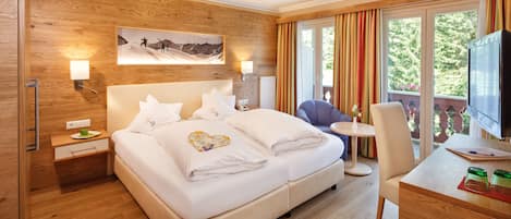 A modern hotel room with a wooden accent wall, a large bed with white linens, a desk with a television, and a balcony with curtains.
