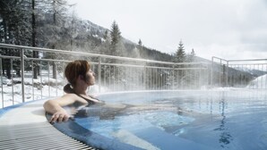 Une personne se détend dans un bain à remous, avec une vue sur des montagnes et des arbres couverts de neige.