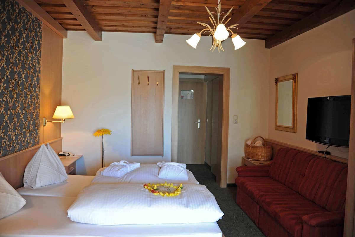 Una habitación de hotel con una cama, un sofá rojo, un televisor y techo de madera.