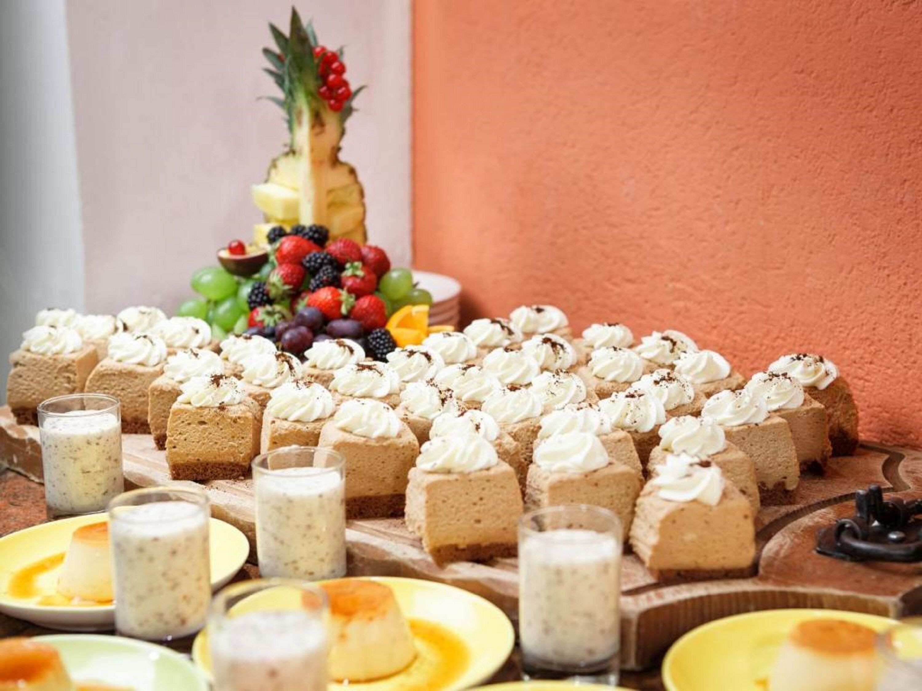 A dessert table with various cakes and pastries, including a pineapple and a fruit arrangement.