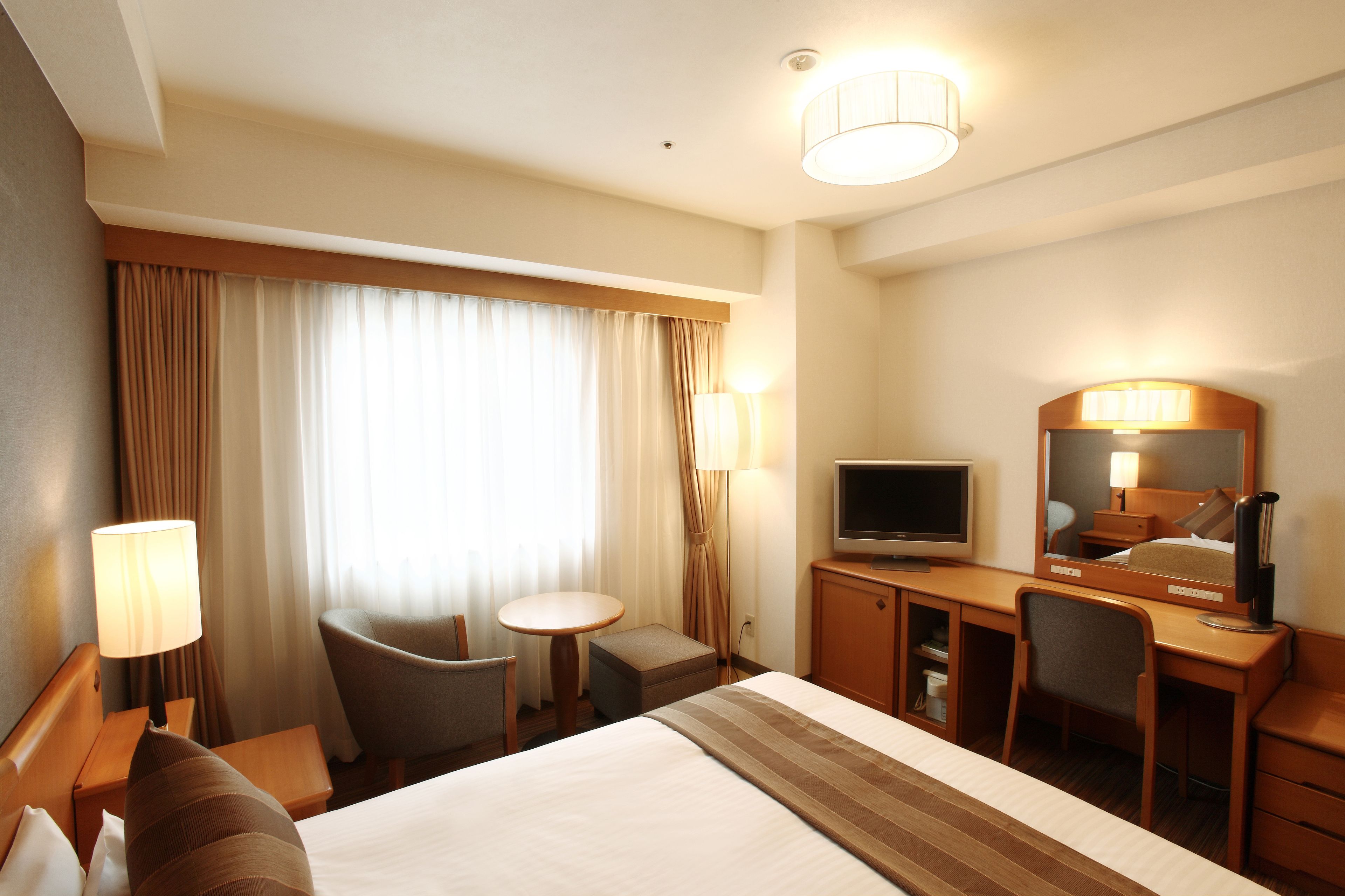 Habitación de hotel con una cama grande, un escritorio con televisor, una silla, una mesita y una lámpara.