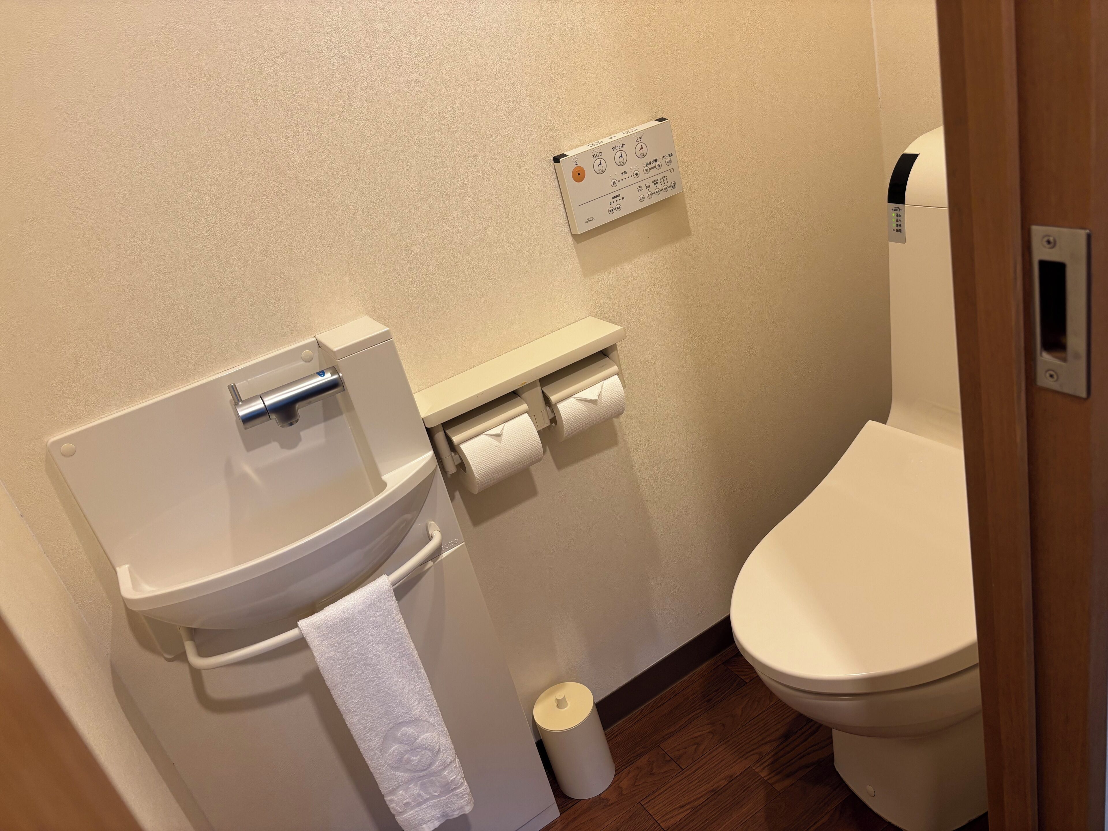 A bathroom with a toilet, a paper towel dispenser, and a toilet paper roll.