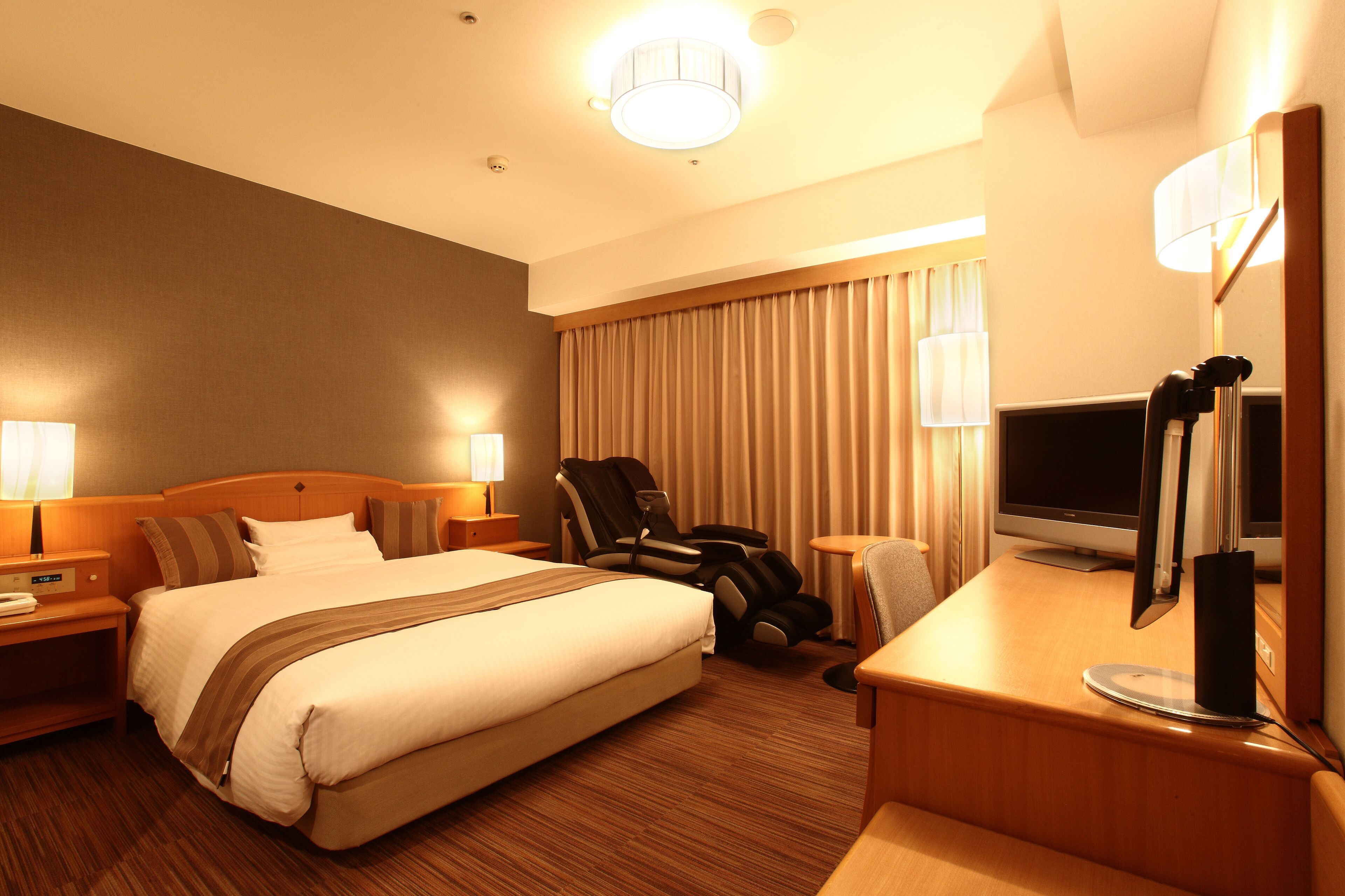A hotel room with a large bed, a desk with a computer, a chair, and a TV.