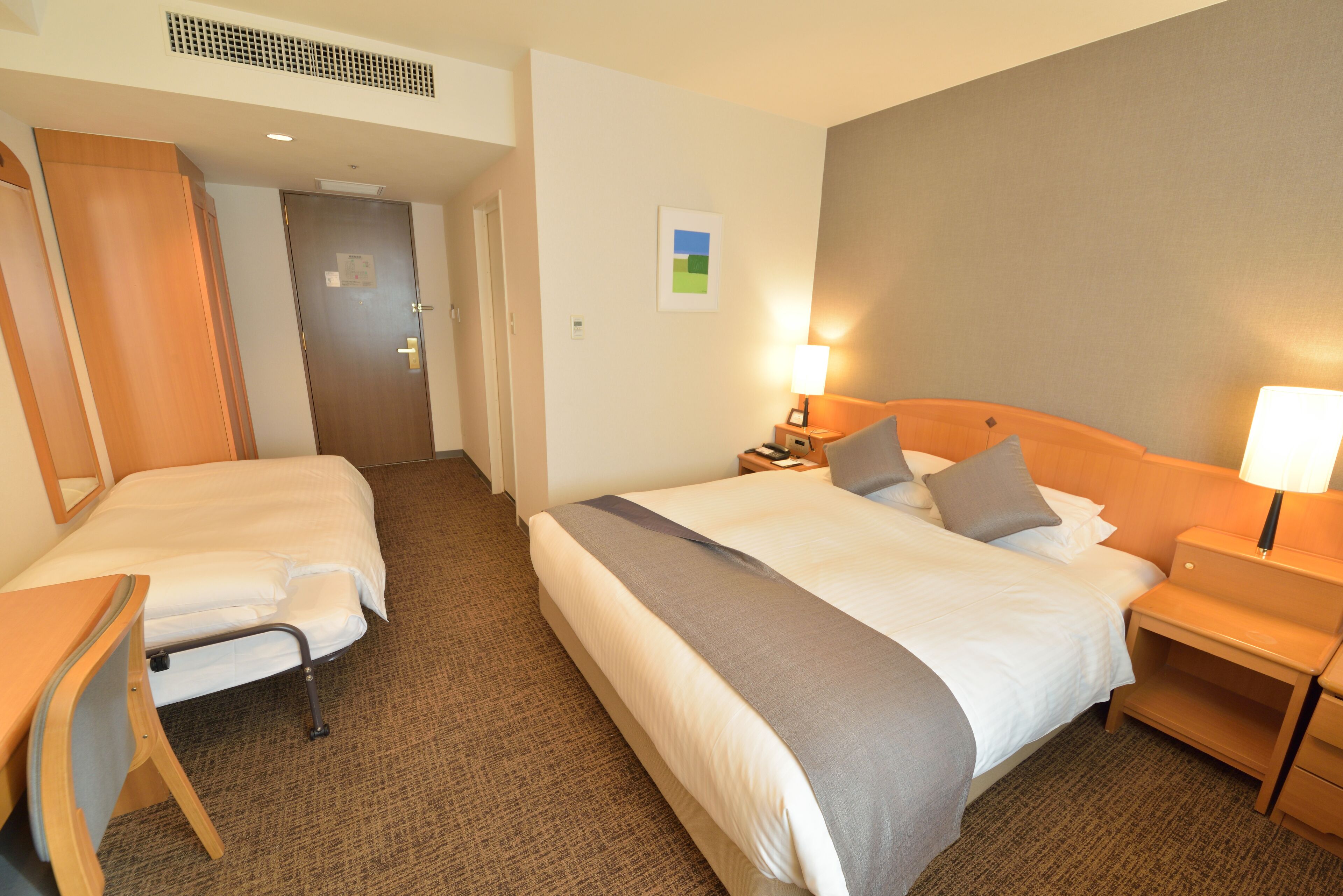 A hotel room with two beds, a desk, and a nightstand with lamps.
