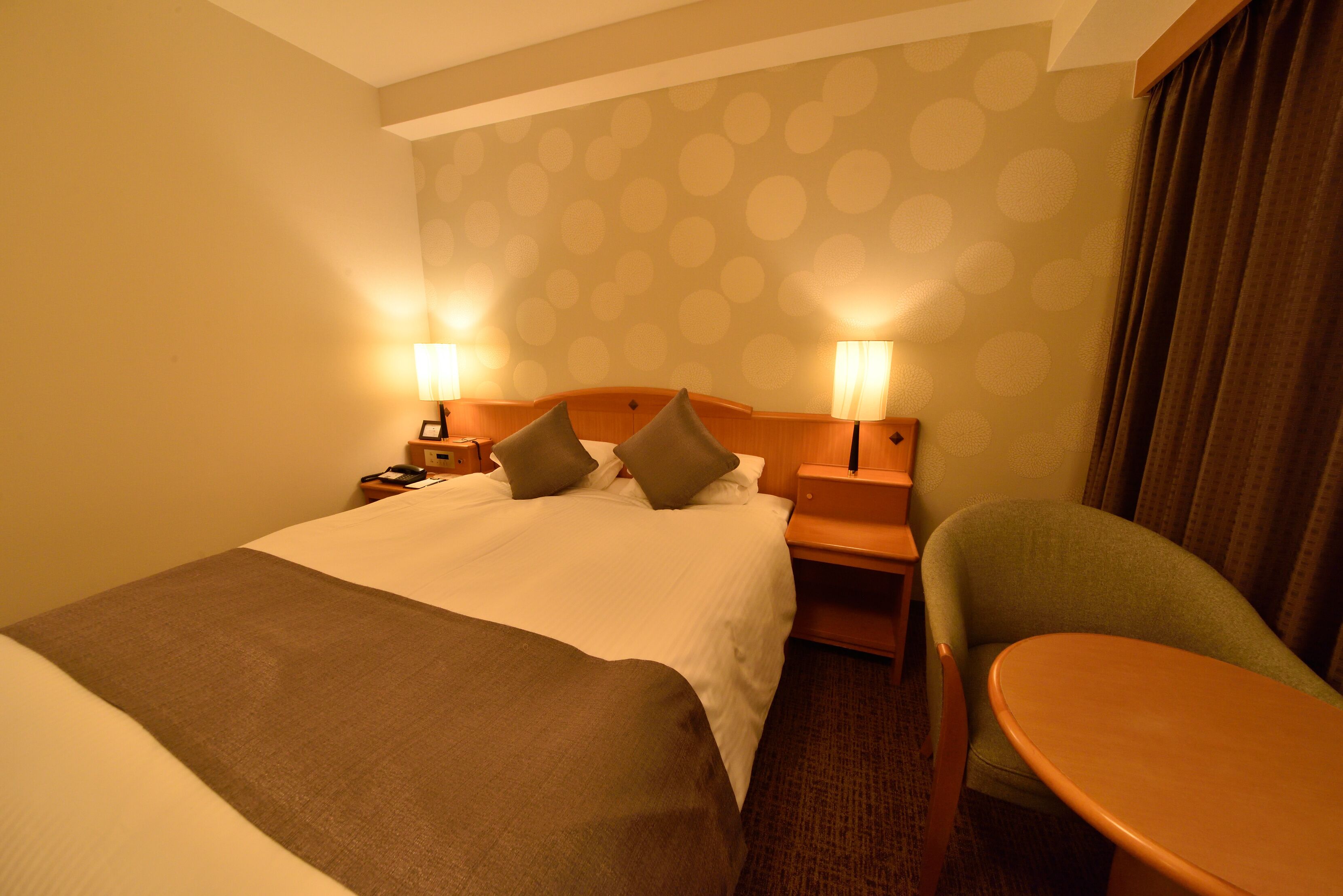 A hotel room with a large bed, two bedside tables with lamps, a green armchair, and a small round table.