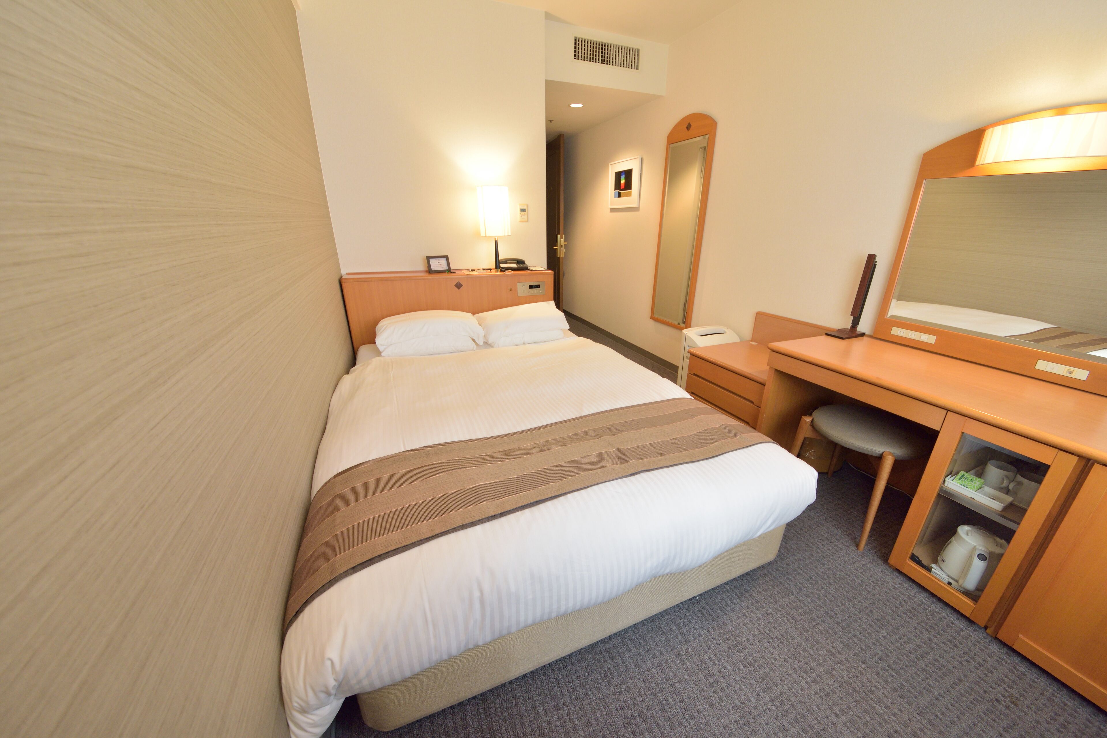 Une chambre d’hôtel avec un lit, un bureau, un miroir et une armoire.
