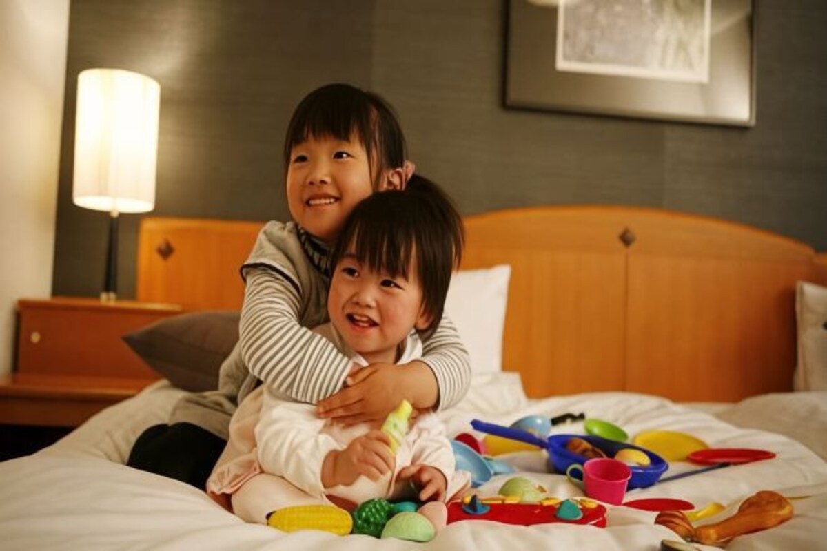 Two children playing with toys on a bed in a hotel room.