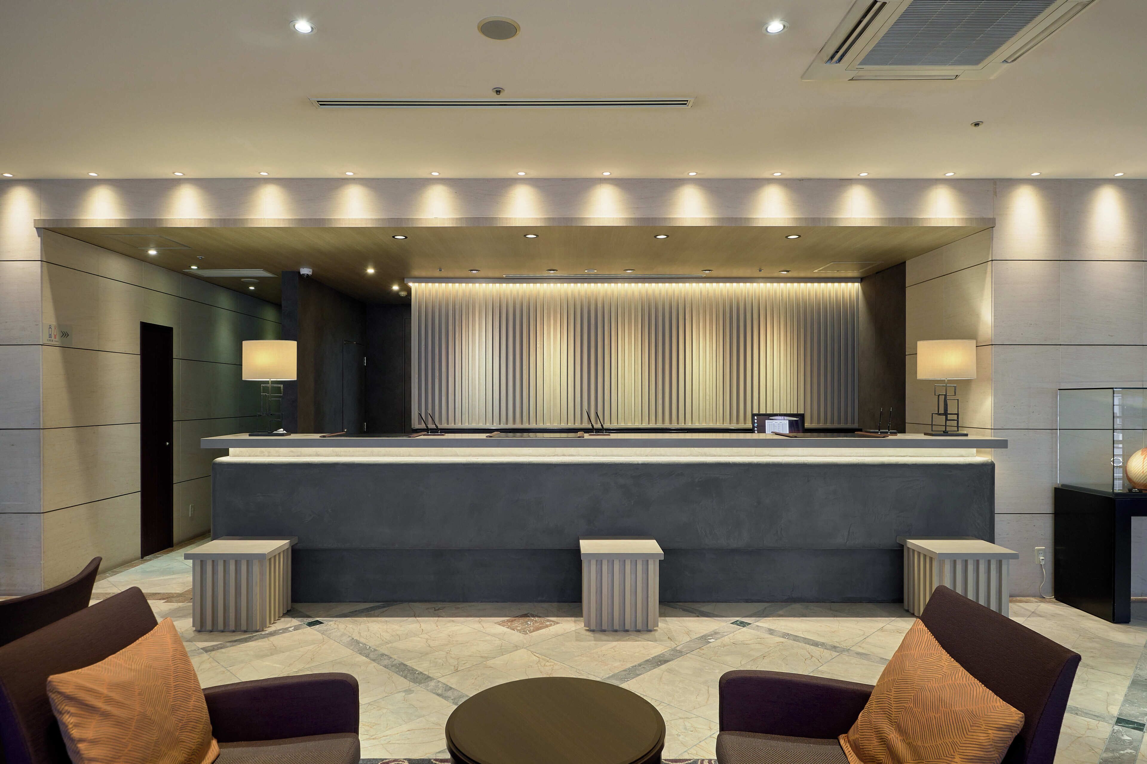 A modern lobby with a reception desk, seating area, and a large mirror.