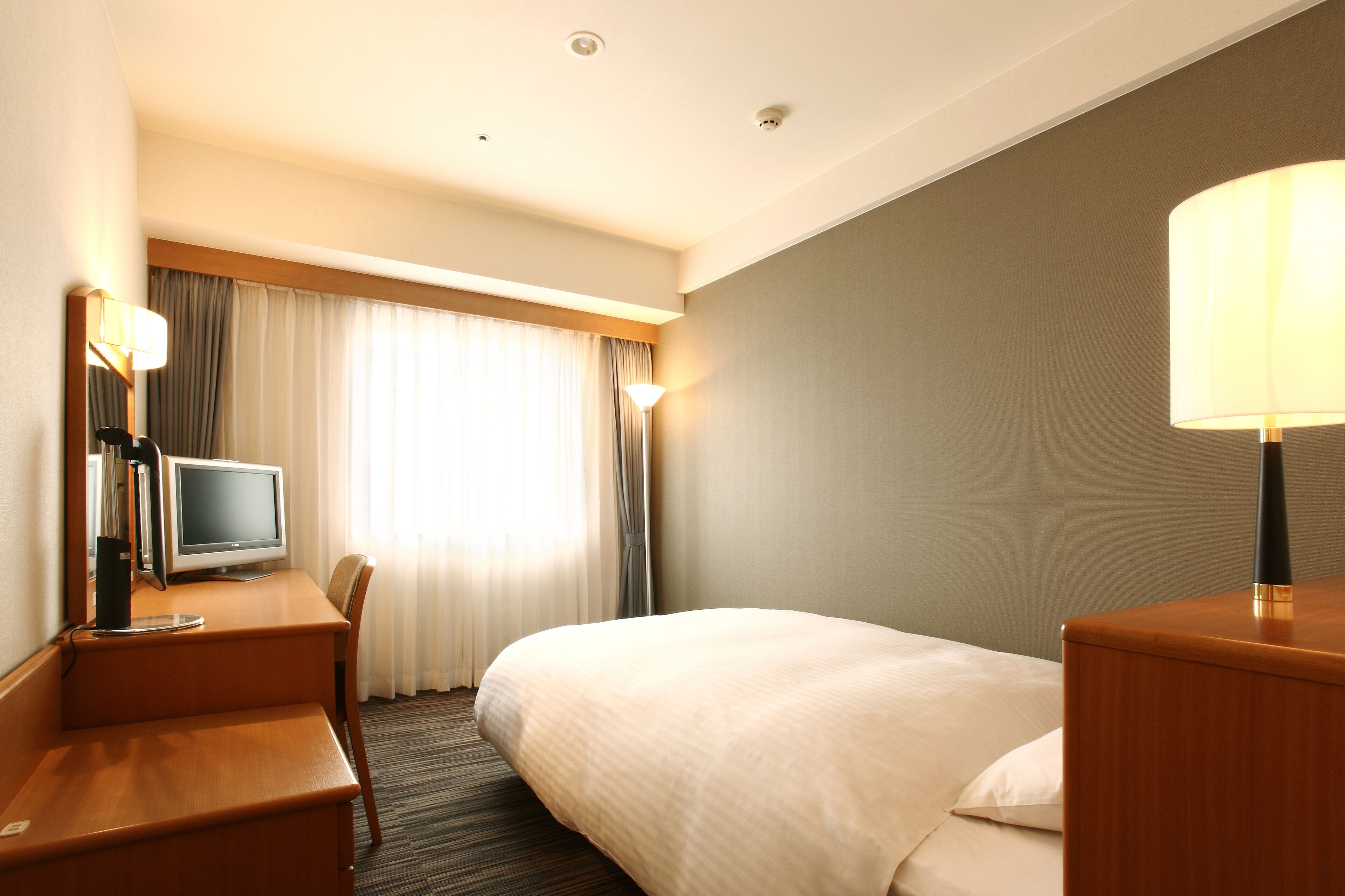 Ein Hotelzimmer mit einem Bett, einem Schreibtisch mit Computer, einem Stuhl und einer Lampe.