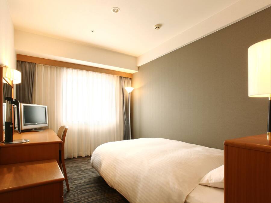 Ein Hotelzimmer mit einem Bett, einem Schreibtisch mit Computer, einem Stuhl und einer Lampe.
