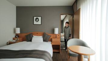 A hotel room with a large bed, bedside tables, a chair, and a small table.