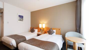 A hotel room with two beds, a small table, and a chair.