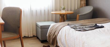 Una habitación de hotel con una cama, una silla, una mesita pequeña y una mesita de noche.