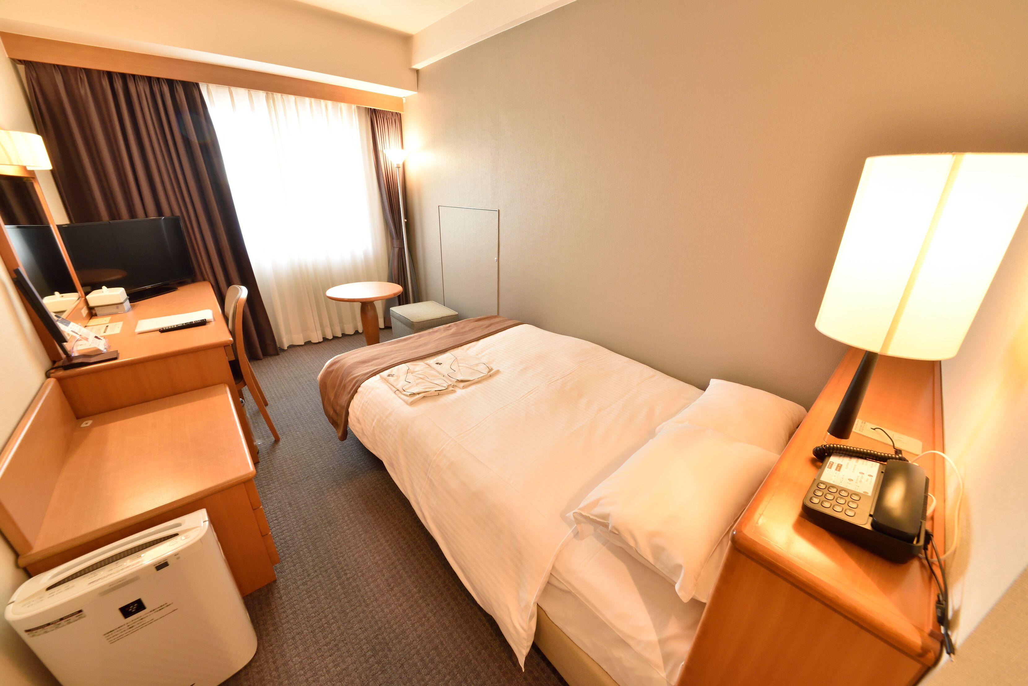 A hotel room with a bed, desk, chair, and a small table.