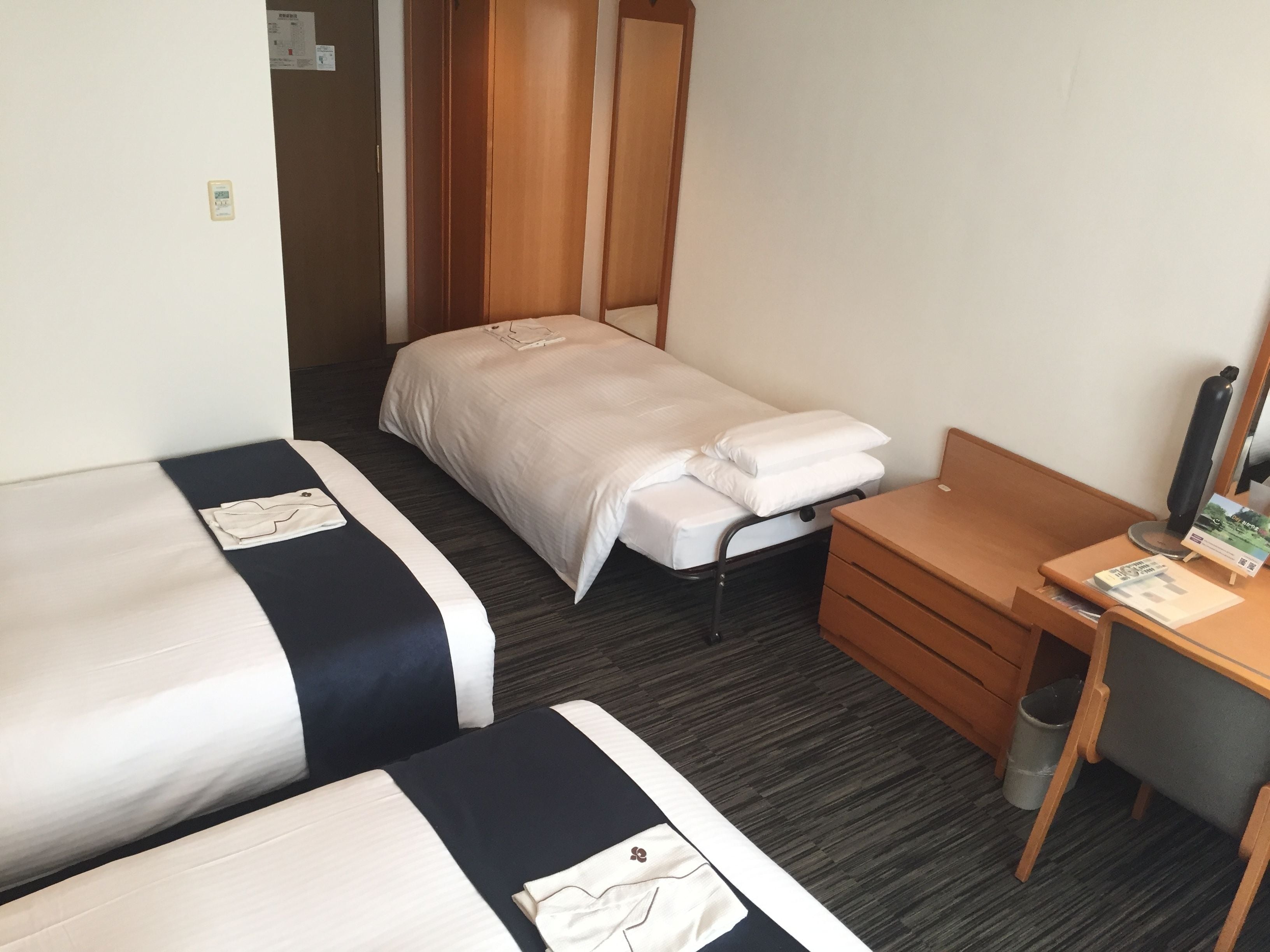 A hotel room with two single beds, a wooden desk, a chair, and a small trash bin.