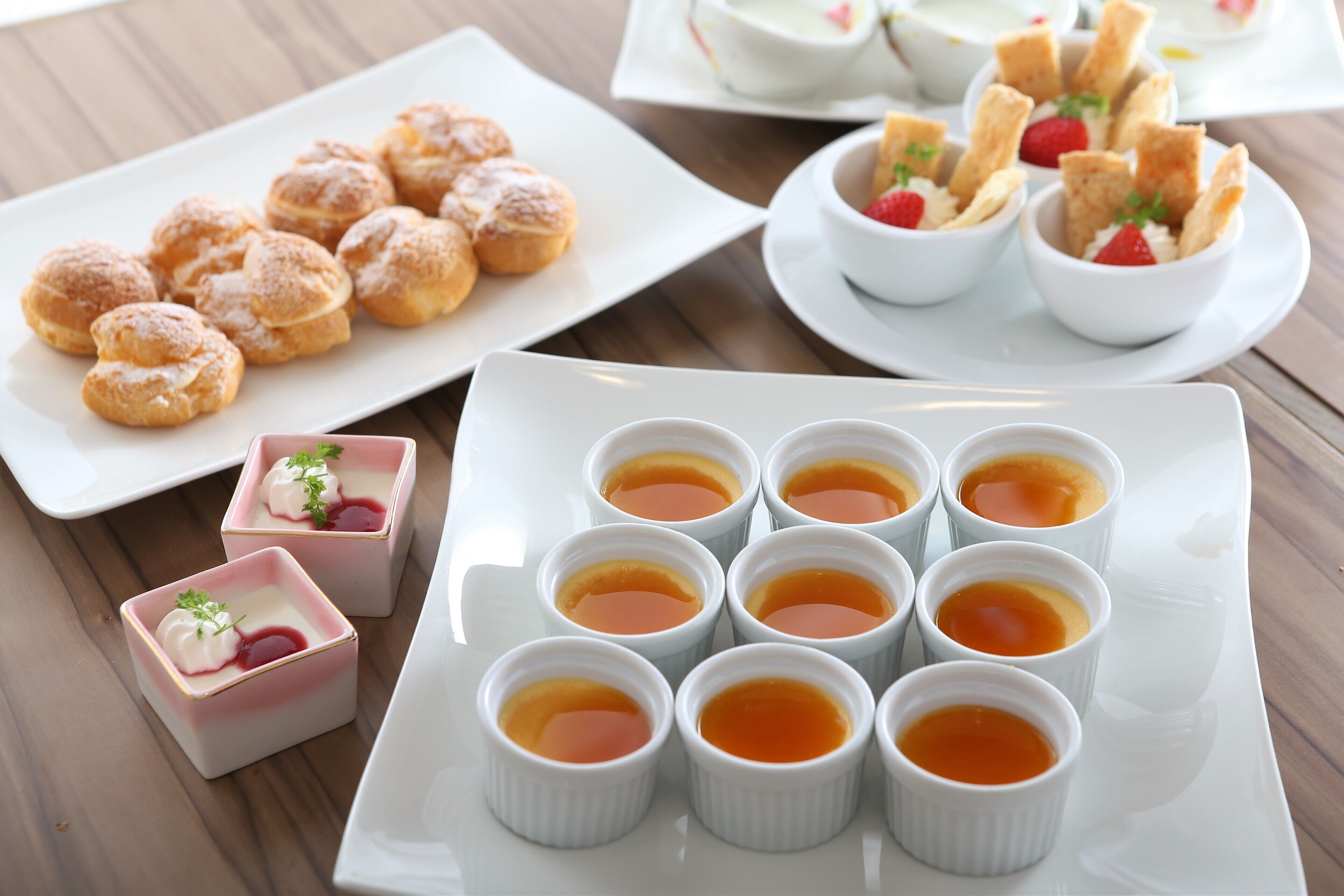 A table with various desserts including cream puffs, a dessert with strawberries, and small cups of a yellow dessert.