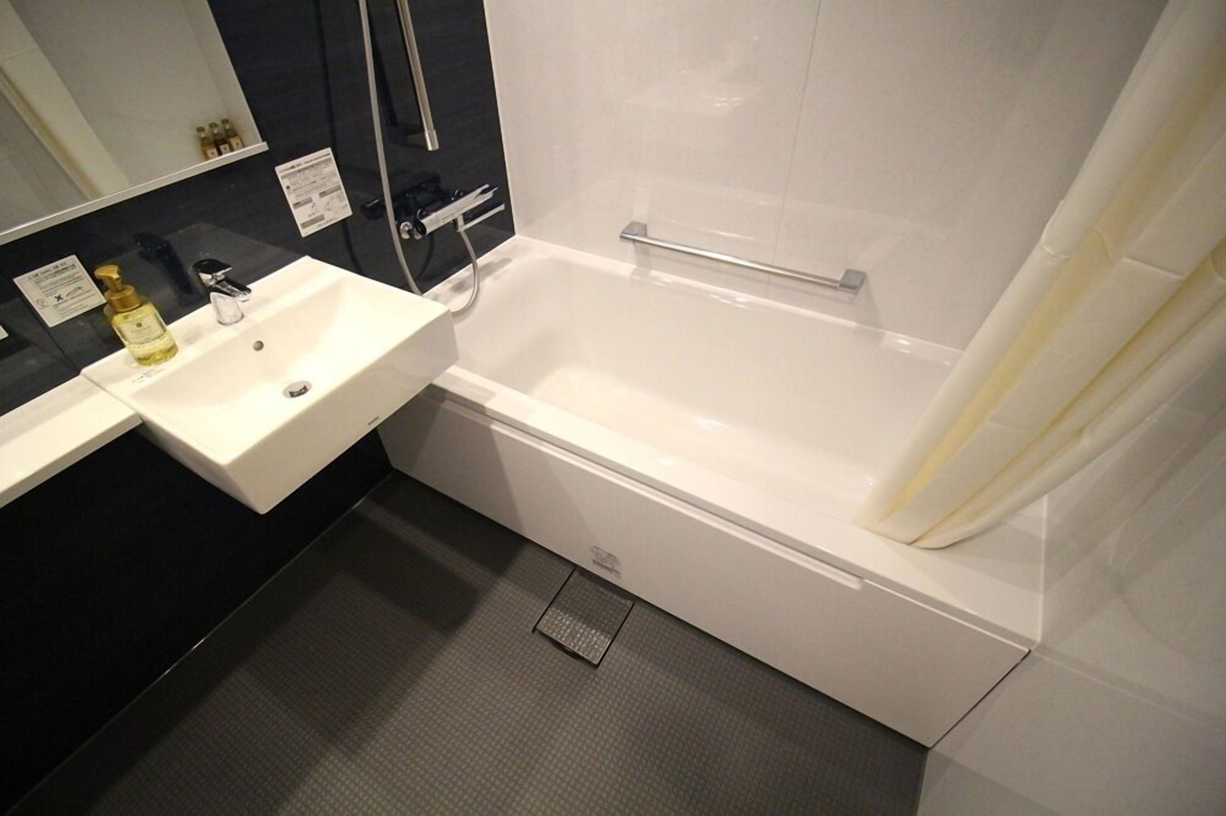 Un baño con una bañera blanca, lavamanos y zona de ducha.