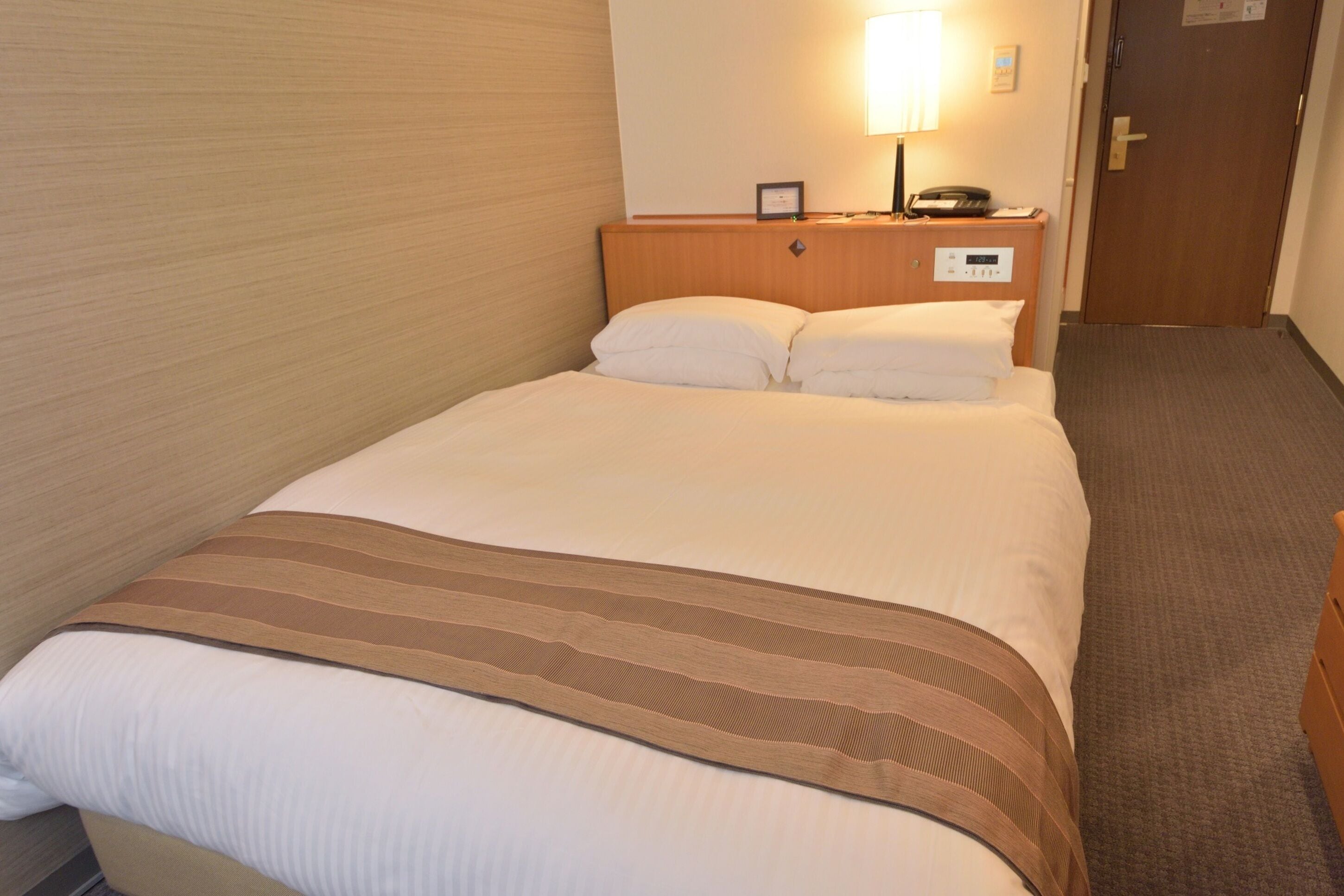 Una habitación de hotel con una cama, una mesita de noche con lámpara y una puerta.