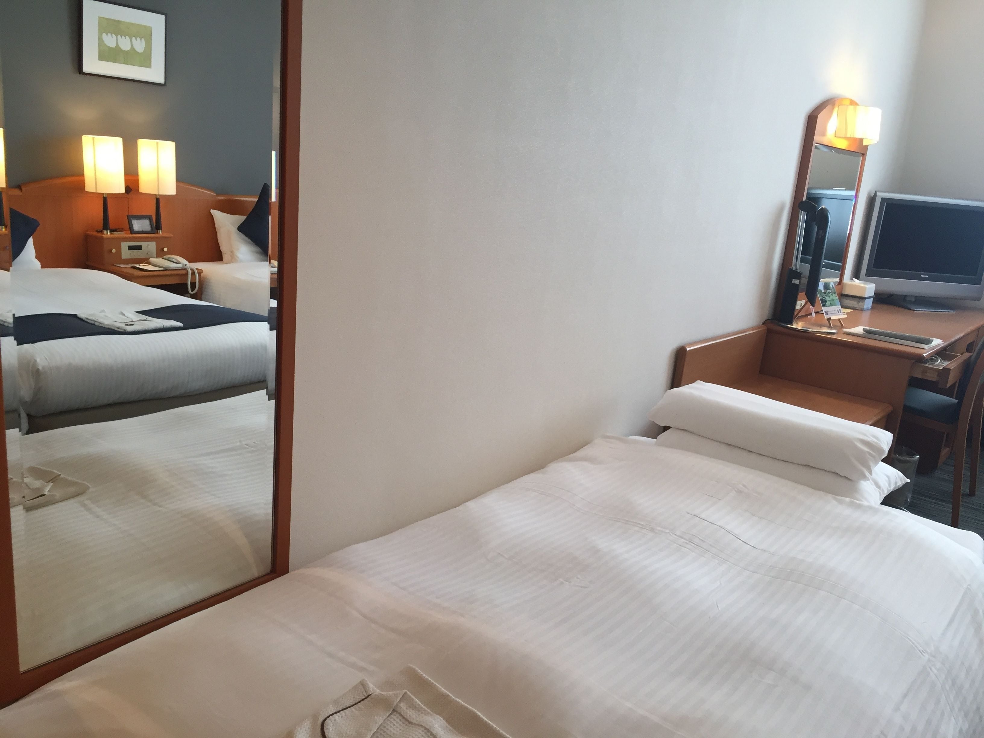 Habitación de hotel con una cama grande, un escritorio con ordenador, una silla, una mesita de noche con lámparas y un espejo.