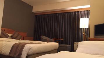 A hotel room with two beds, a desk, a chair, a TV, and a lamp.