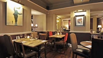 A restaurant interior with wooden tables and chairs, candle centerpieces, and framed artwork on the walls.