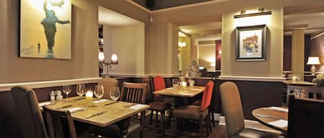 Interior de restaurante con mesas y sillas de madera, centros de mesa con velas y cuadros en las paredes.