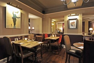 Interior de restaurante con mesas y sillas de madera, centros de mesa con velas y cuadros en las paredes.