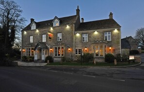 A stone building with multiple windows and a signboard, likely a hotel or inn, with a well-maintained lawn and a paved driveway. - The Royal George Birdlip by Greene King Inns (Gloucester)